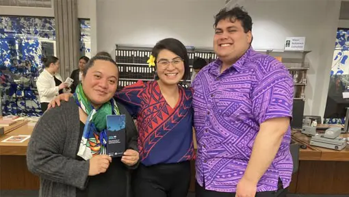 Three people pose for a photograph while smiling at the camera and wearing colourful patterned shirts. 