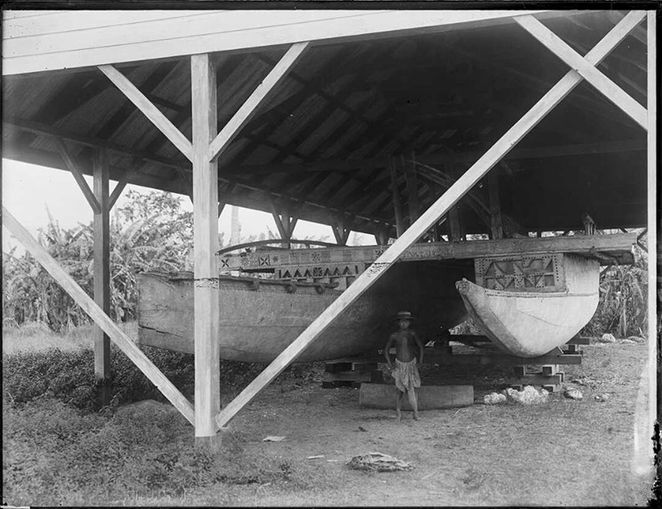 Boy standing in front of a big double hull canoe.
