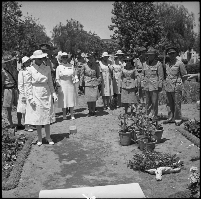 Women and men wearing white and khaki uniforms stand at the cemetery.