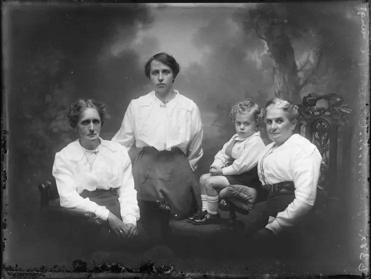 A formal black and white portrait of three women and a small child, all wearing white tops. 