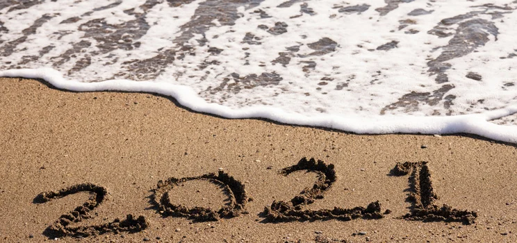 Waves approaching the numbers 2021 in sand.