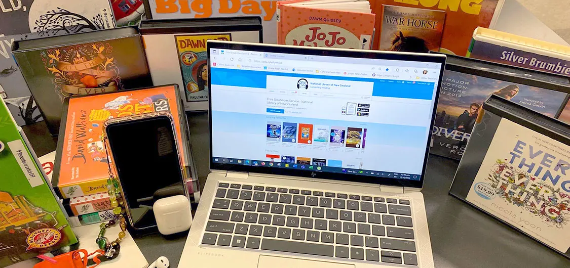 Audiobooks from the Print Disabilities Service are on display alongside a laptop with the Print Disabilities Service Wheelers ePlatform on the screen.