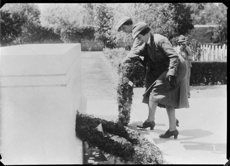 Two women place a wreath upon the memorial in the cemetery.