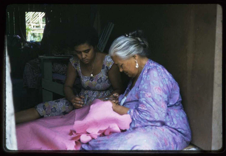Two women sitting on the ground sewing. 