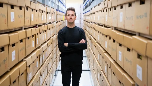 A man standing arms crossed between two walls of archive boxes.