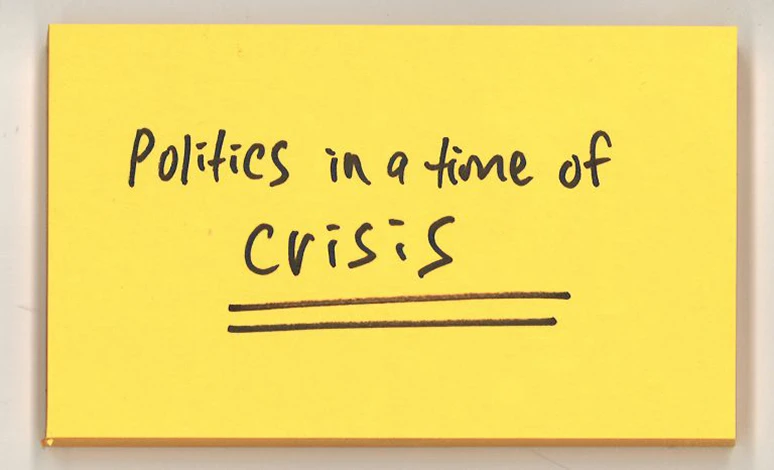 Post-it note with words "Politics in a time of crisis" written on it.