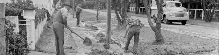 Two men use shovels to move silt off the pavement. 