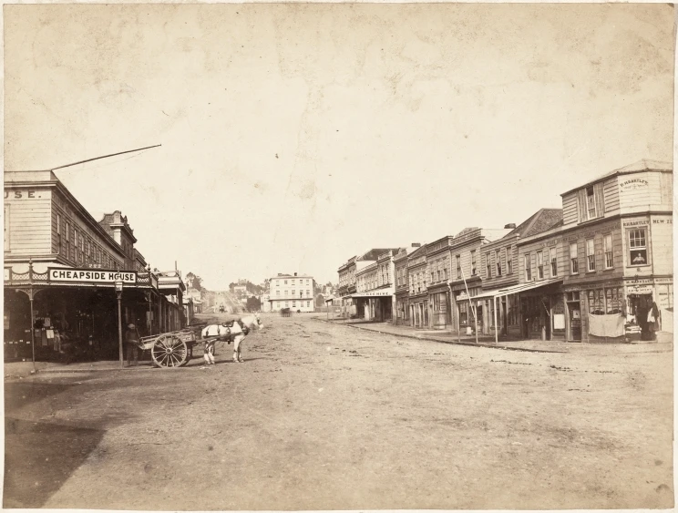 A faded, black and white photograph of an intersection with wooden buildings on both sides of a street and horse and buggy.
