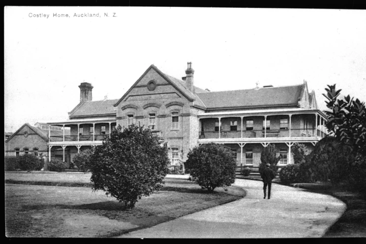 A black and white photo of a large two-story brick building with verandahs running along the entire front façade and a driveway leading to the front door with a man walking towards the entrance.