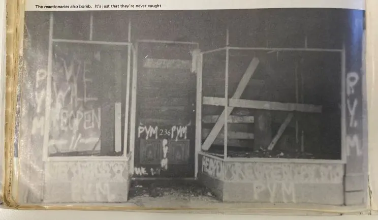 A black and white image showing the charred remains of a bookstore with boarded-up door and windows and spraypainted words across the front that read, "PYM. WE WILL REOPEN". 