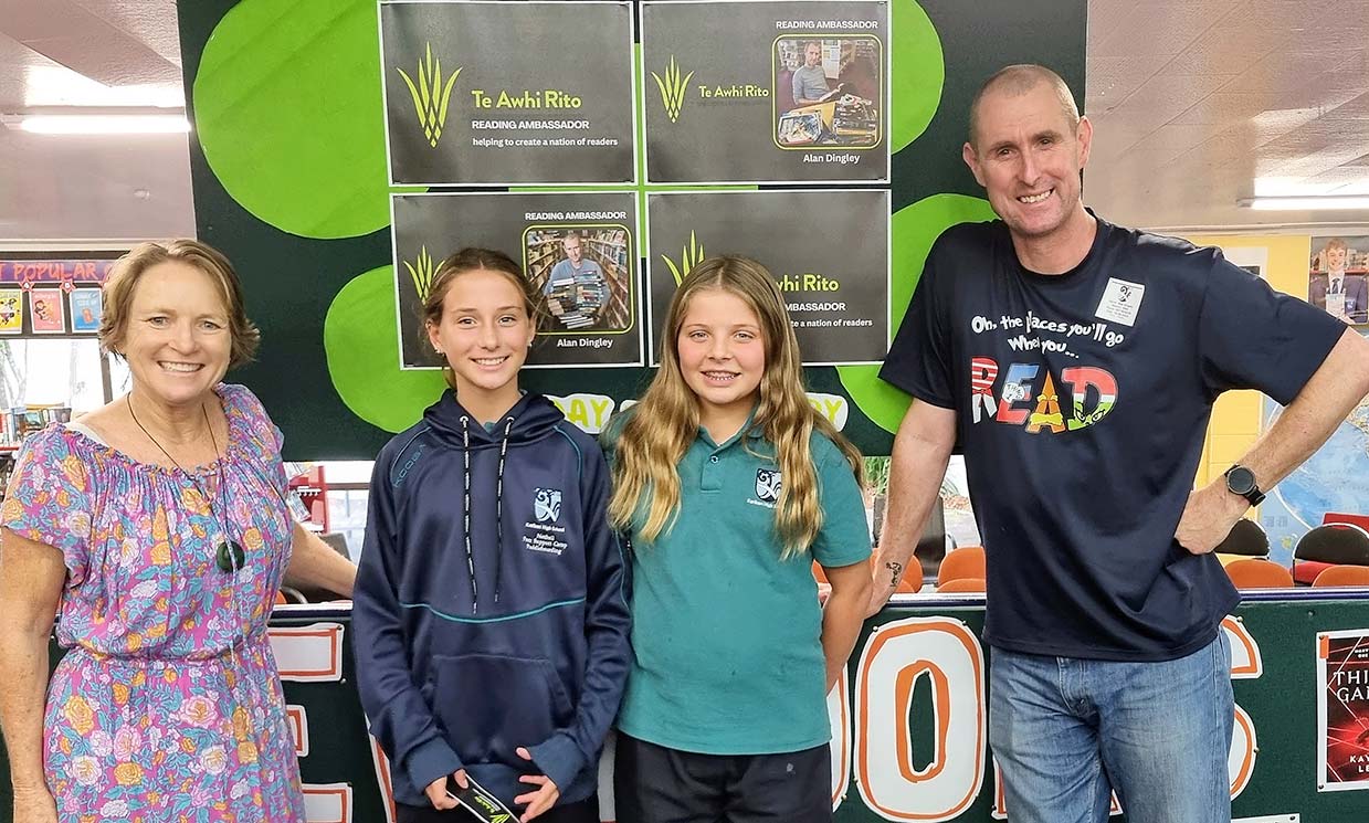 Group photo of Julia Smith and 2 students from Kerikeri High School with Alan Dingley — all smiling and standing in front of a display with Te Awhi Rito posters.