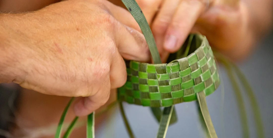 Photo of hands weaving a small, green flax basket.