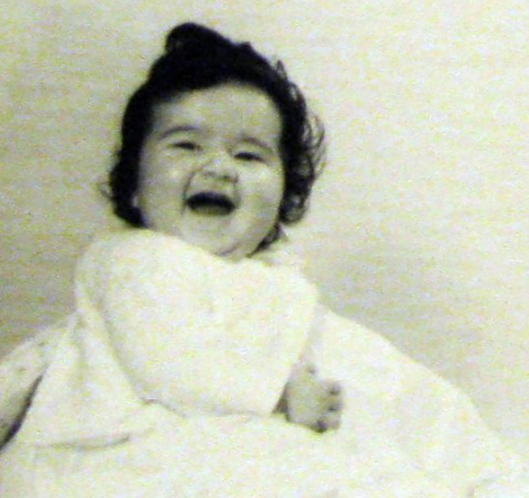 Photo of a happy laughing baby in a white gown. 