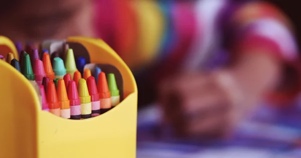 A child colouring beside rainbow coloured crayons.