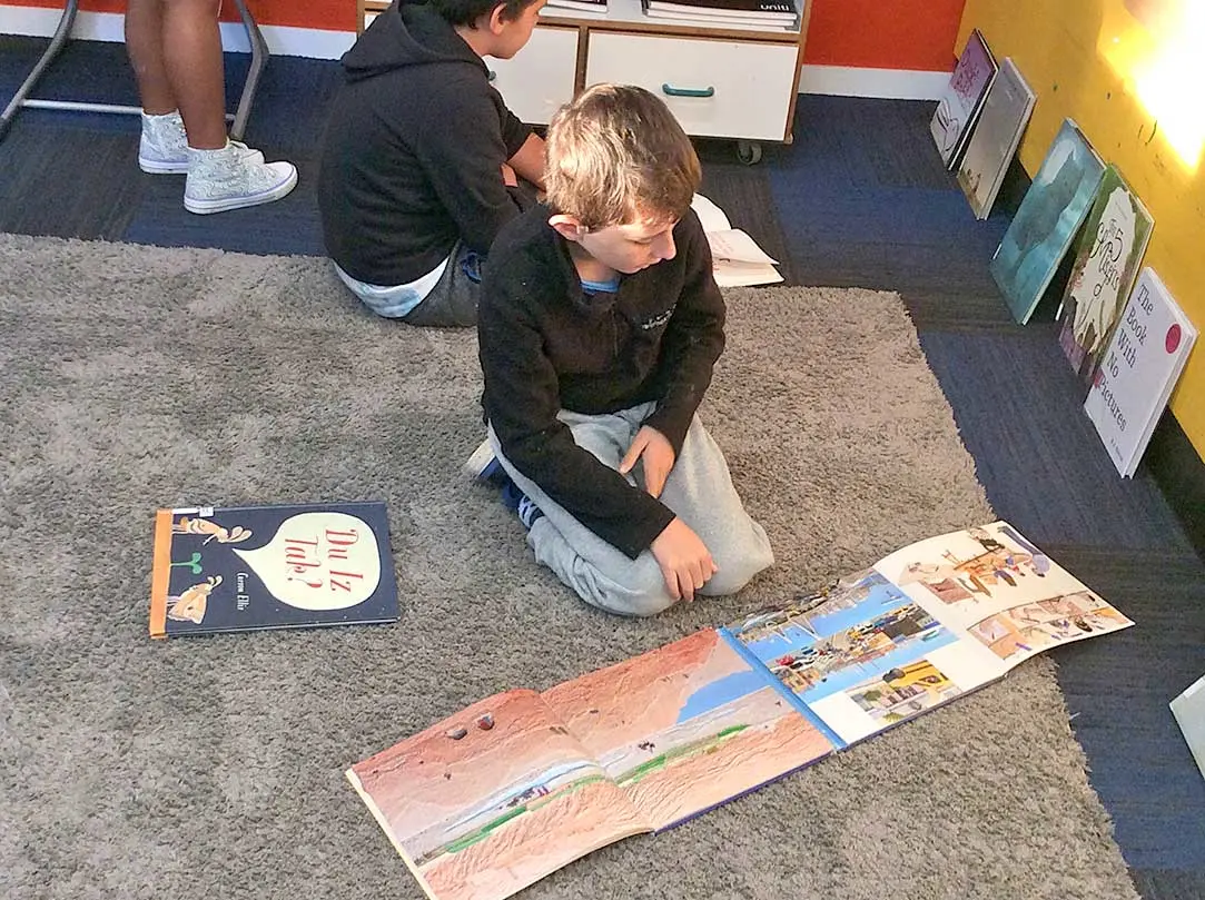 Tamariki reading picture books on a classroom floor. The photo focuses on a tamariki looking at 2 books open next to each other.