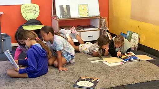 A group of students reading picture books together on a classroom floor.