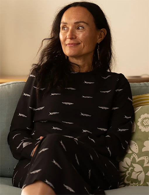 Portrait of a smiling Māori woman sitting on a couch.