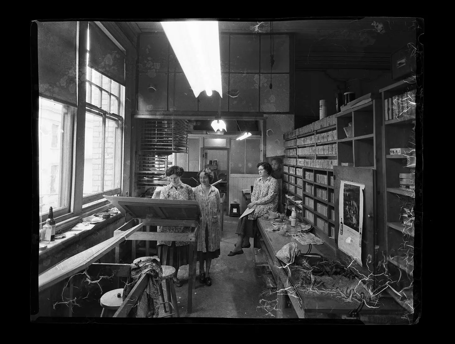 Black and white photo of 3 female Whites Aviation staff in a studio. 1 staff member is working on a drafting table while the other 2 watch.