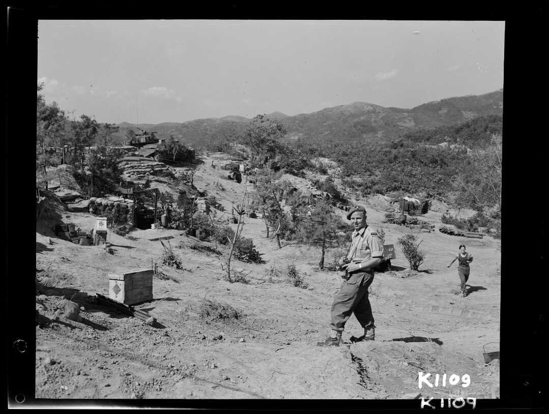 Shows Mackley standing in arid, hilly terrain wearing combat uniform.