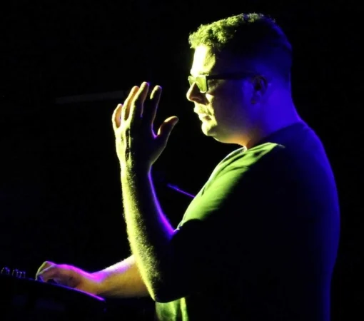 A man is silhouetted on stage while playing an electronic instrument. 
