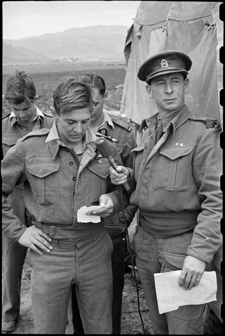 Four soldiers standing outside an army tent. One of the soldiers holds a microphone.