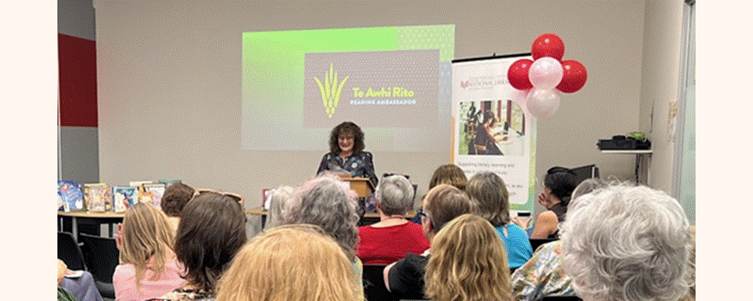 Kate De Goldi presenting at a National Library 60th birthday celebration event, with the audience seated and red and white balloons decorating the venue.