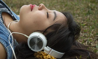 Girl lying on the grass with eyes closed, listening with headphones.