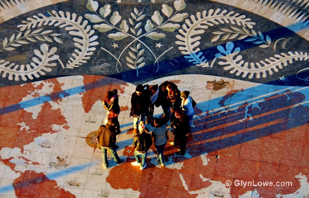 A group of individuals standing on a world map with the routes of famous Portuguese explorers at the Sea Discoveries Monument in Lisbon.