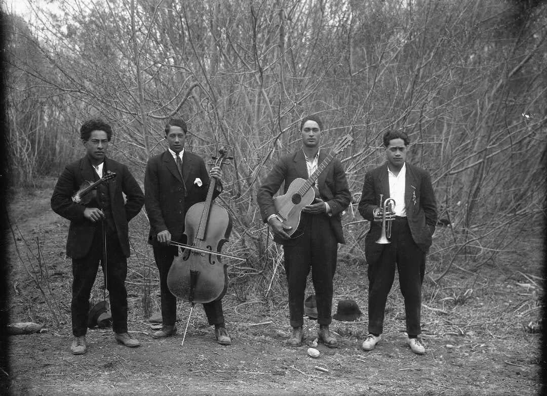 Four Māori men holding string and brass instruments.