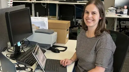 A woman seated at a computer workstation is seen smiling. 