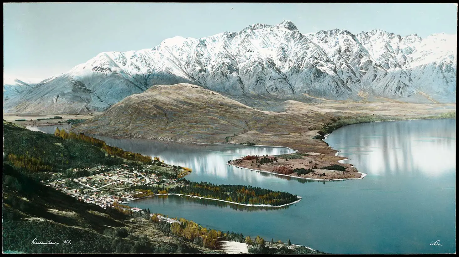 Hand-coloured photo showing an aerial view of Queenstown, Lake Wakatipu and surrounding mountains.