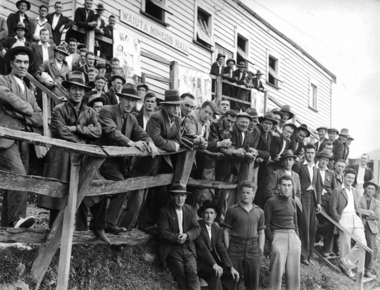 Black and white photo of a large group of miners standing out front of the wooden 'Miners Hall'.