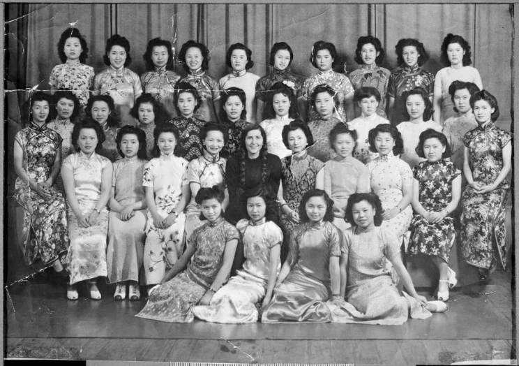 A formal group portrait with four rows of women, those in the front are sitting on the ground, all are wearing traditional dresses.