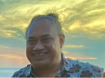 Smiling Polynesian man, there is a beautiful sunset in the background. 