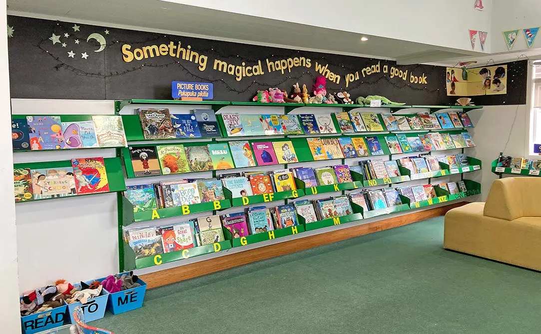 Picture books on wall shelves in a school library. There is a banner with the words 'Something magical happens when you read a good book'.