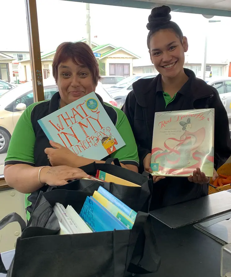 Two smiling Māori women holding books.