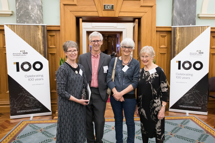 Group photo of four people smiling at the camera outside the door to the Grand Hall.