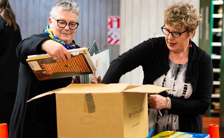 Two women taking children's books out of a cardboard box