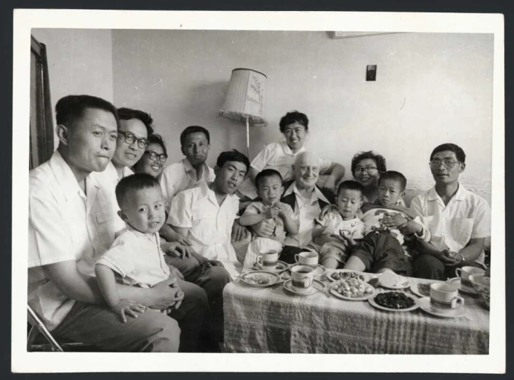 An informal group portrait in a dining room with people of all ages surrounding a table with food.