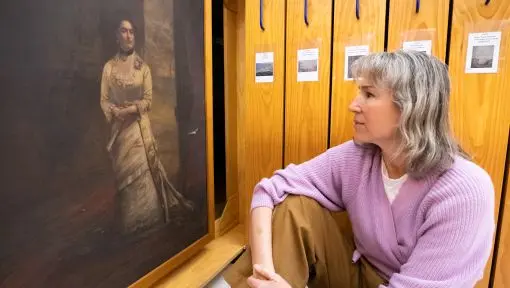 A woman observes a painting that is being held in a wooden archival storage device.