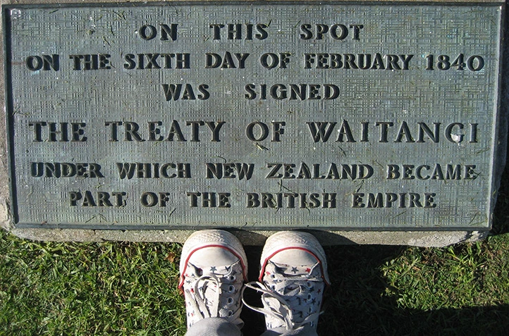 Sneakers of a young person standing next to a plaque that reads: 'On this spot on the sixth day of February 1840 was signed The Treaty of Waitangi under which New Zealand became part of the British Empire'.