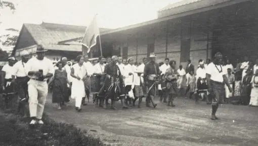 A group of people are seen marching together along a dirt road. 