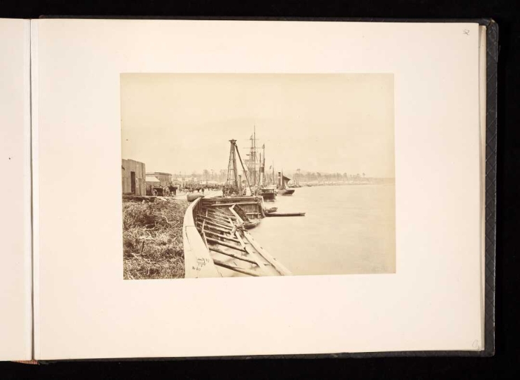 At the edge of the water in Hokitika township with wooden jettys and sailing ships at dock.