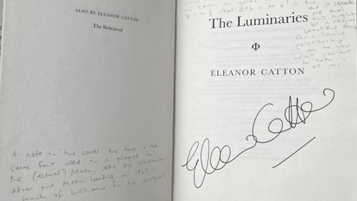 An author's signature is seen in black ink on the title page of their novel along with notes written in pencil in the margin.