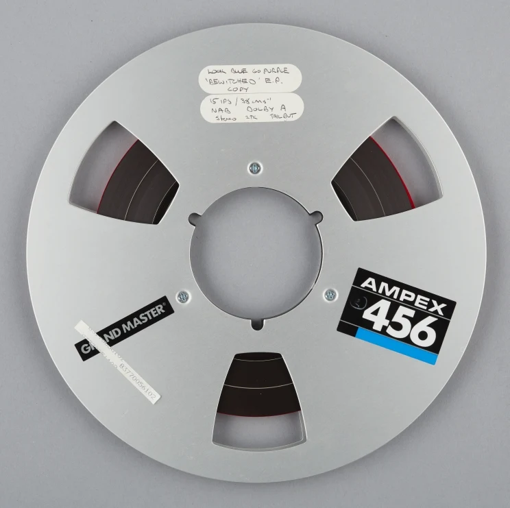 Magnetic tape reel with small hand written labels affixed to the front and the words, 'Ampex 456' and 'Grand master'