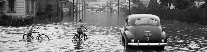 A car and two children on bicycles in a flooded street. 