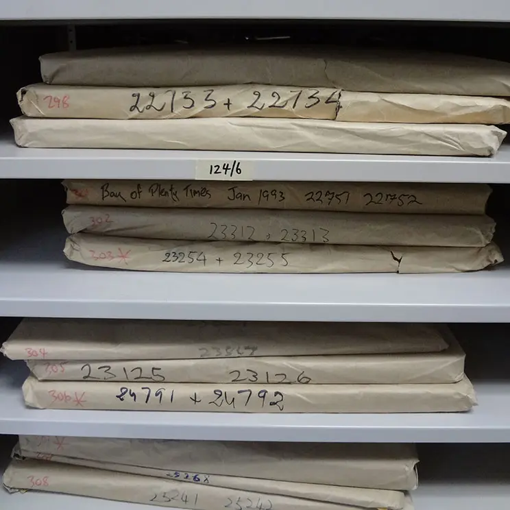 Newspapers wrapped in paper with handwritten notes on the spine of the package on shelves at Wairere House. 