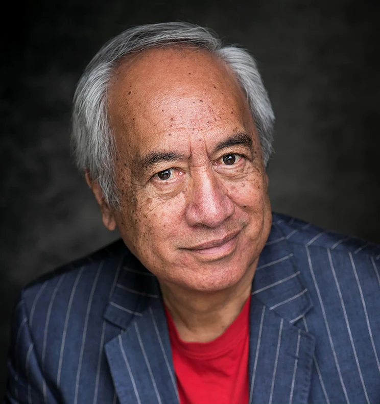 Author Witi Ihimaera wearing a pinstriped blazer and a red t-shirt.