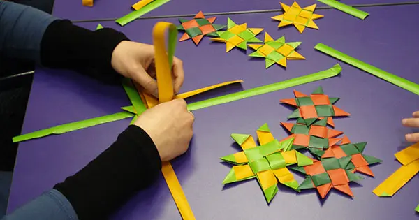 A person weaving a Matariki star with paper.