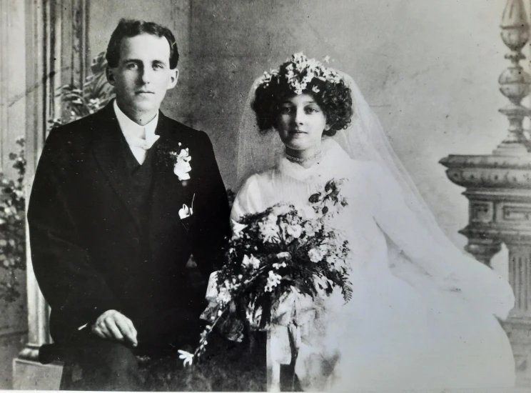 A black and white wedding photo of a man and woman wearing formal dress and holding flowers.
